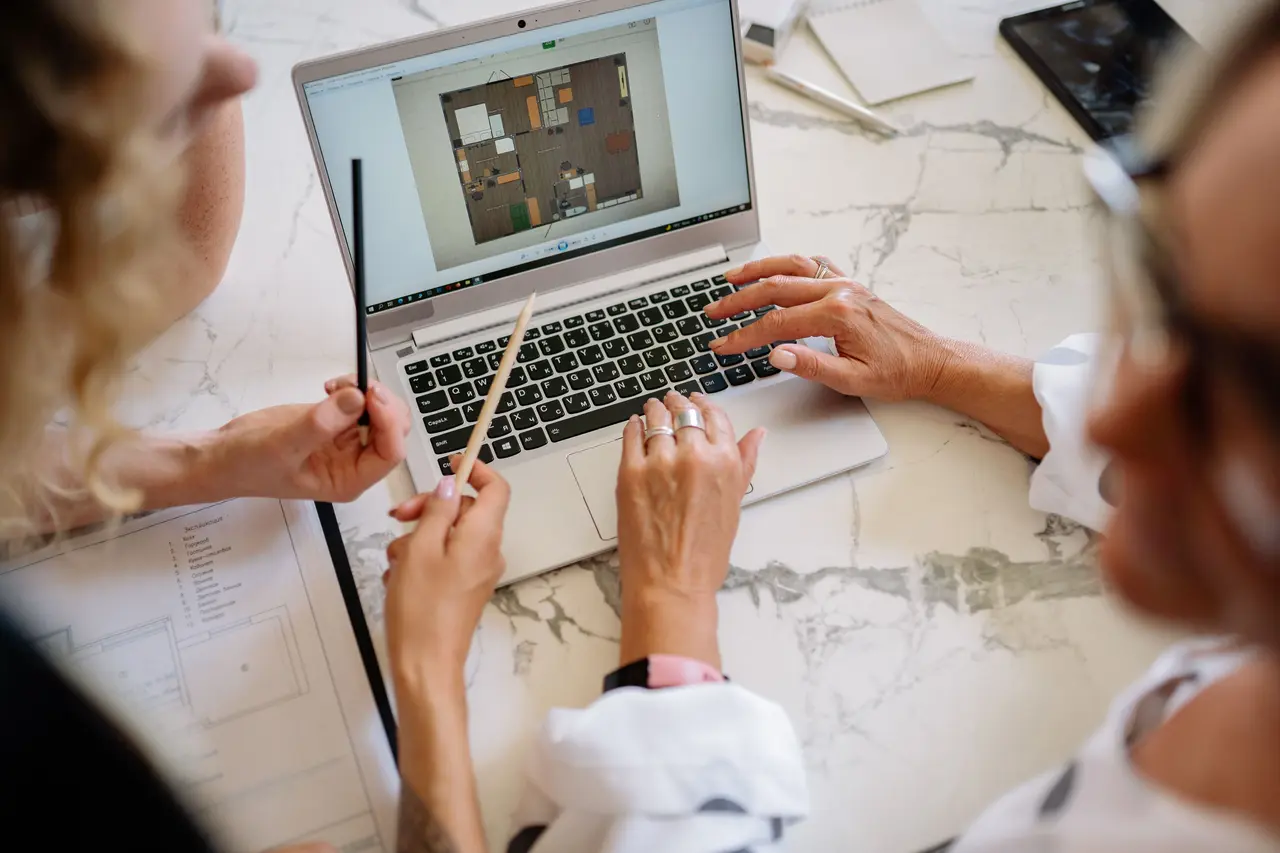 Ontwerpers vergelijken een 3D-meubelindeling op een laptop met afgedrukte plattegronden