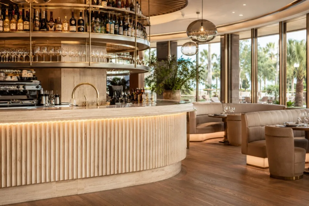 Bar en lounge in de horeca met een geribbeld stenen aanrechtblad, ronde messing rekken en zitbanken