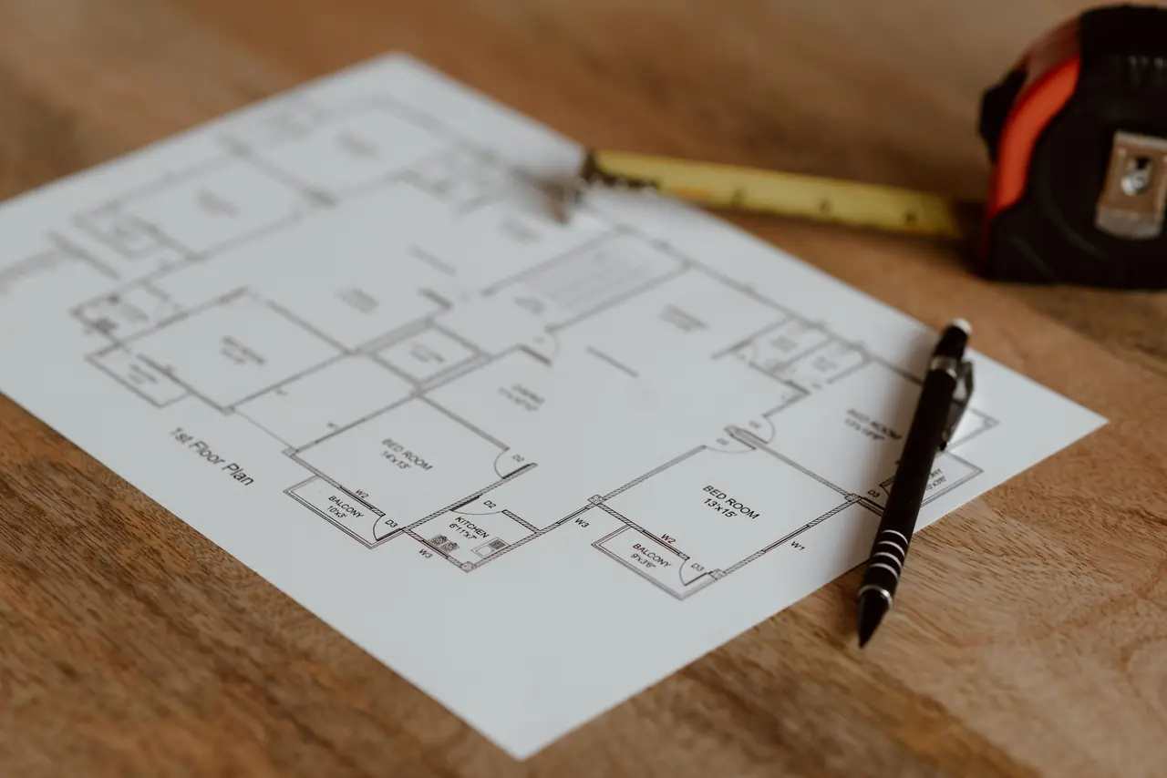 Plattegrond op een houten bureau met een pen en een meetlint voor het ontwerpen van een woning