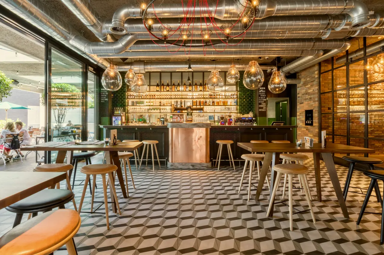 Café-bar met een toonbank met koperen front, zichtbare leidingen en geometrische vloertegels