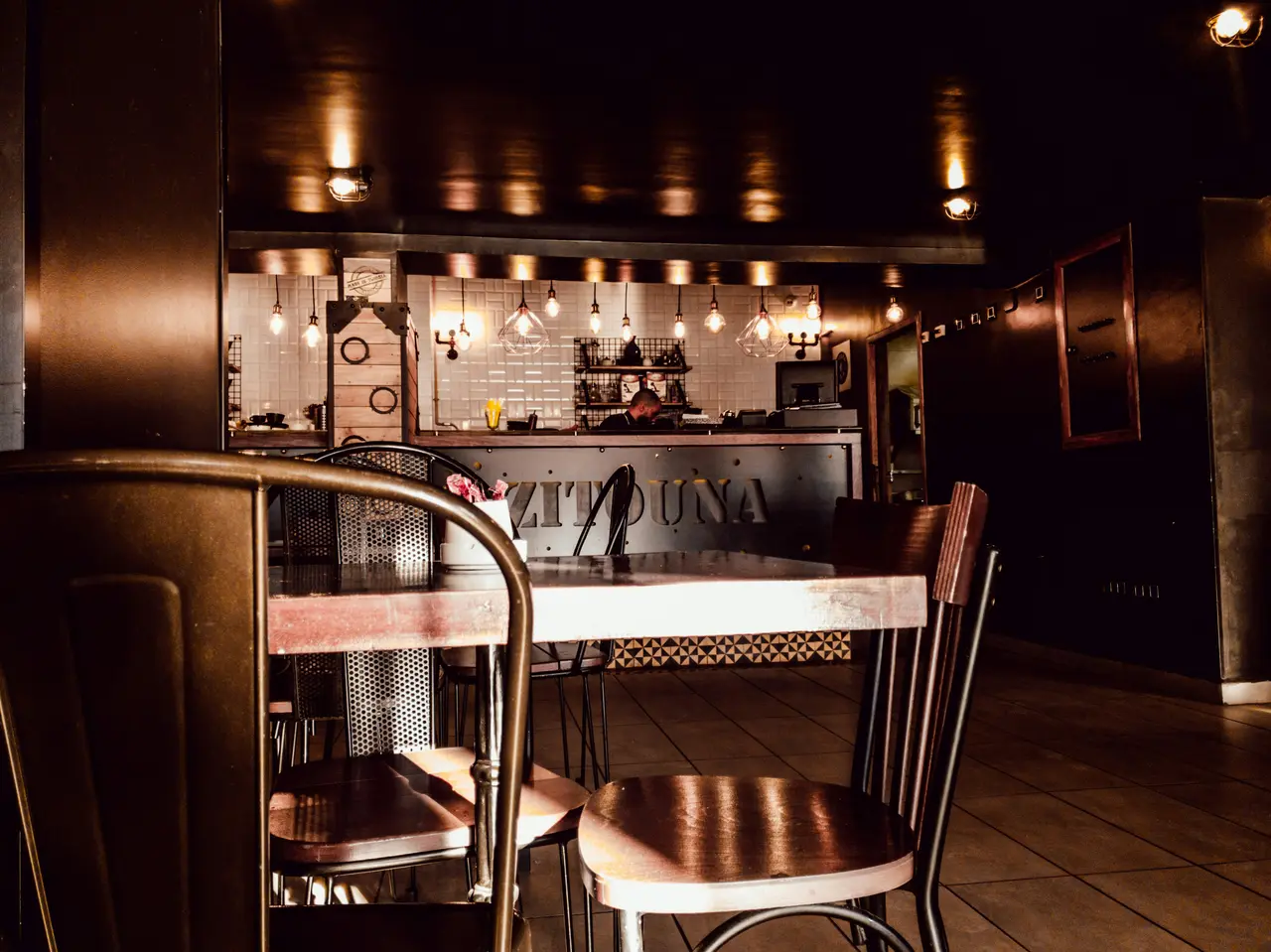 Compact café-interieur met metalen stoelen, donkere afwerkingen en een verlichte bedieningsbalie