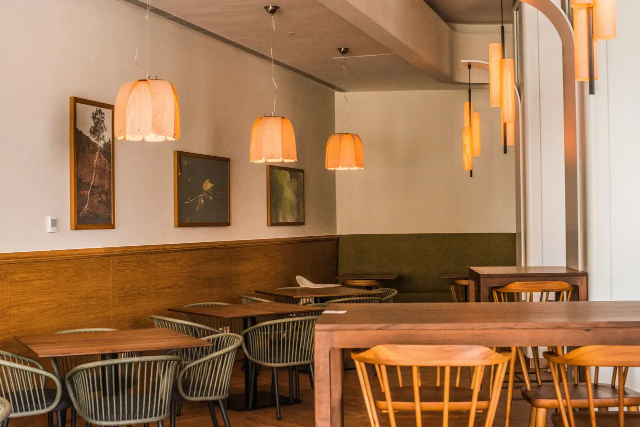 Caféopstelling met houten tafels, geweven stoelen, een bank en warme hanglampen
