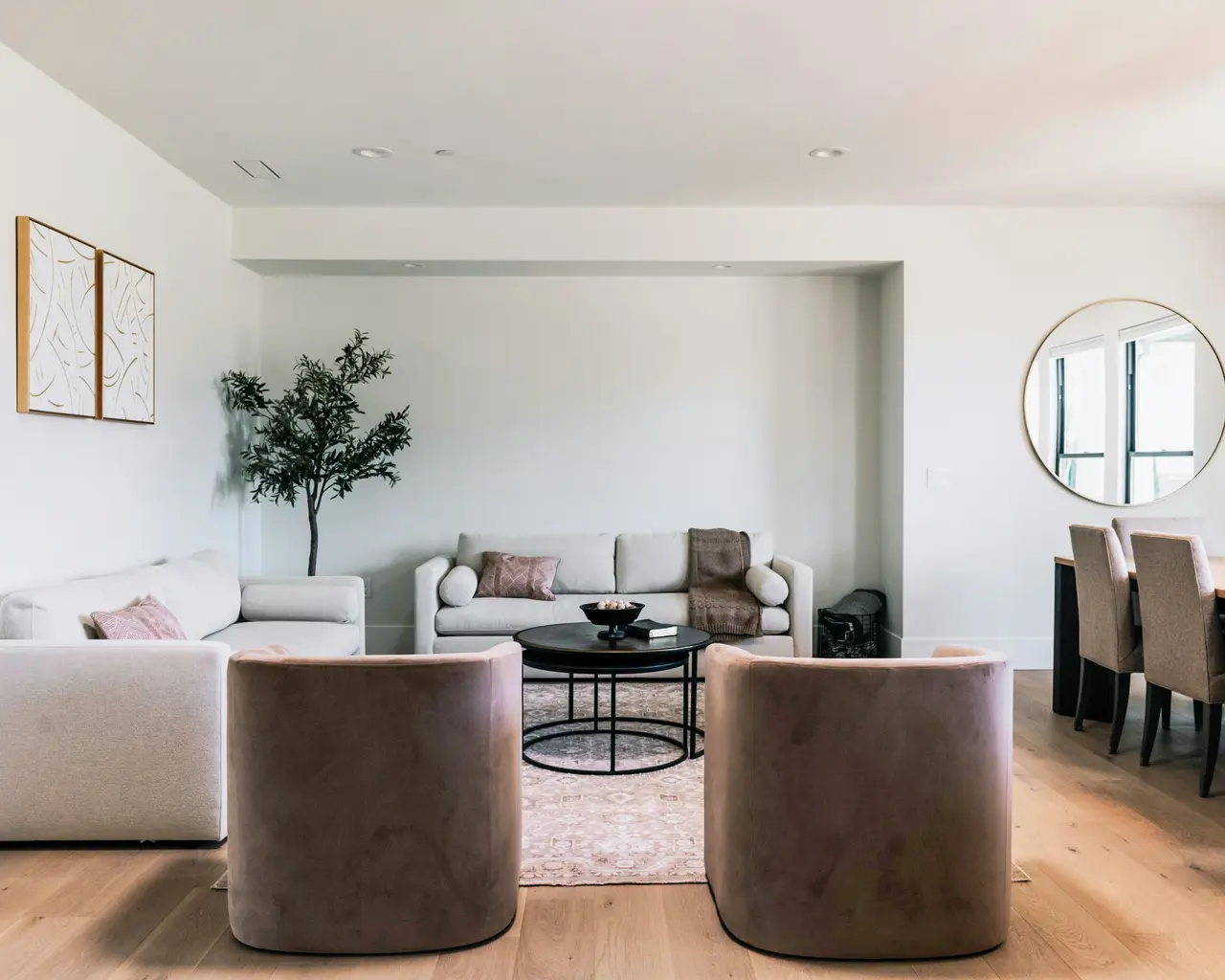 Lichte woonkamer met tegenover elkaar geplaatste banken, fluwelen stoelen, een ronde spiegel en een lichte houten vloer